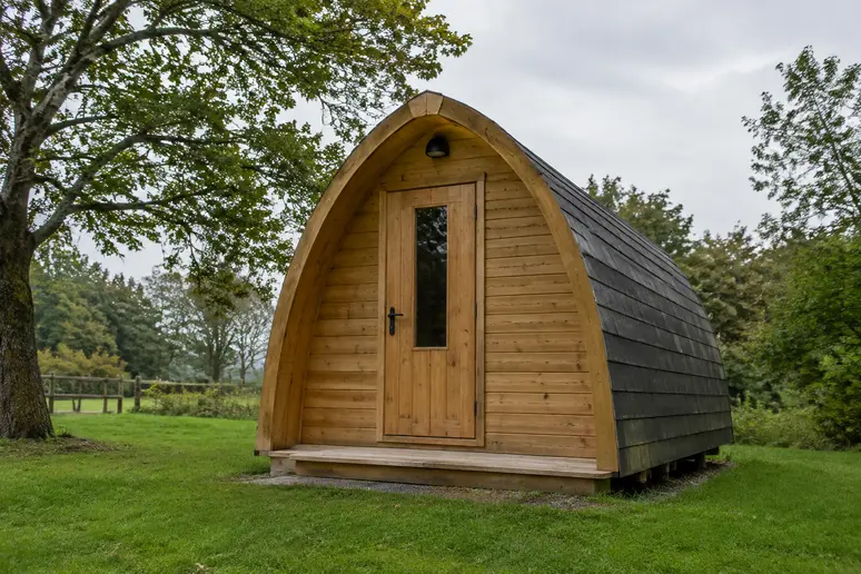 Pod de camping en bois avec structure arrondie installé sur un emplacement herbeux