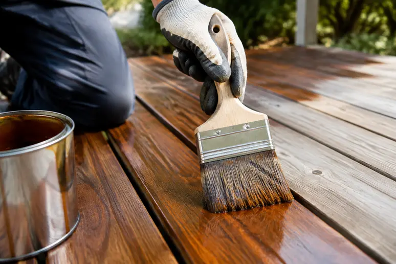 Application d'un saturateur bois au pinceau sur les lames d'une terrasse extérieure.