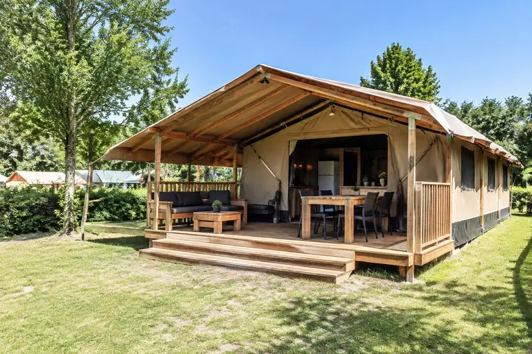 Grande tente lodge de camping avec sa terrasse en bois installee sur un emplacement verdoyant