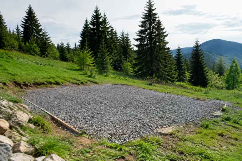 Base en gravier stabilisée préparée sur un terrain avant la pose du tonneau habitable.